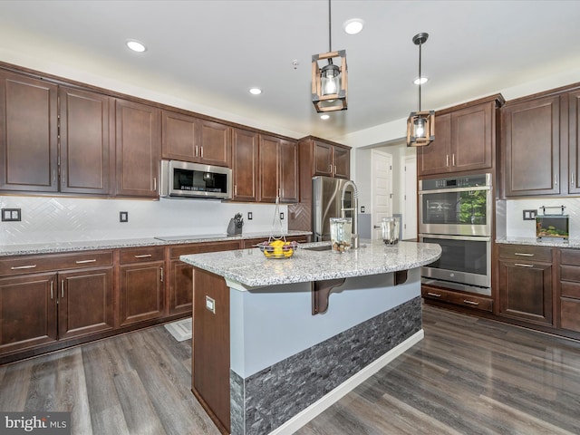 kitchen with pendant lighting, appliances with stainless steel finishes, dark hardwood / wood-style flooring, sink, and a center island with sink