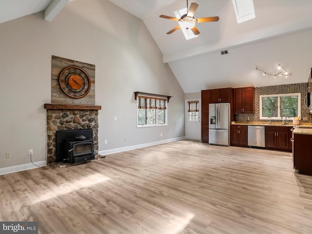 unfurnished living room with high vaulted ceiling, light hardwood / wood-style flooring, a skylight, and ceiling fan