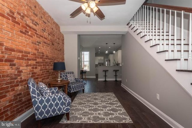 sitting room with dark wood-type flooring, brick wall, and ceiling fan