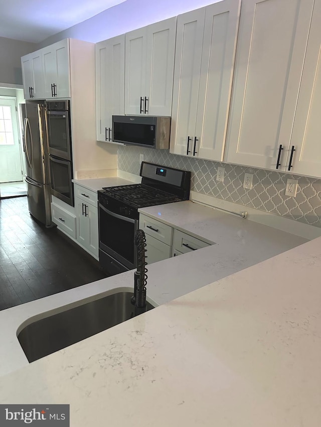 kitchen featuring appliances with stainless steel finishes, white cabinetry, decorative backsplash, sink, and light stone counters