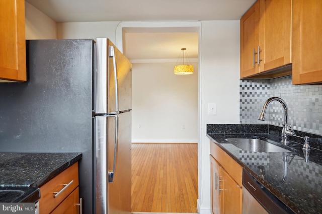 kitchen featuring dark stone counters, tasteful backsplash, hanging light fixtures, sink, and light hardwood / wood-style flooring