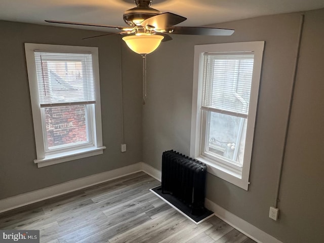 empty room featuring ceiling fan, a wealth of natural light, radiator heating unit, and light hardwood / wood-style floors