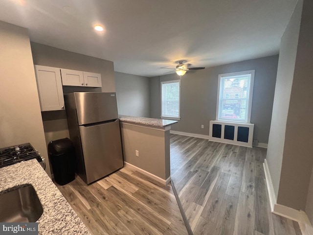 kitchen featuring light stone countertops, white cabinetry, kitchen peninsula, stainless steel refrigerator, and ceiling fan