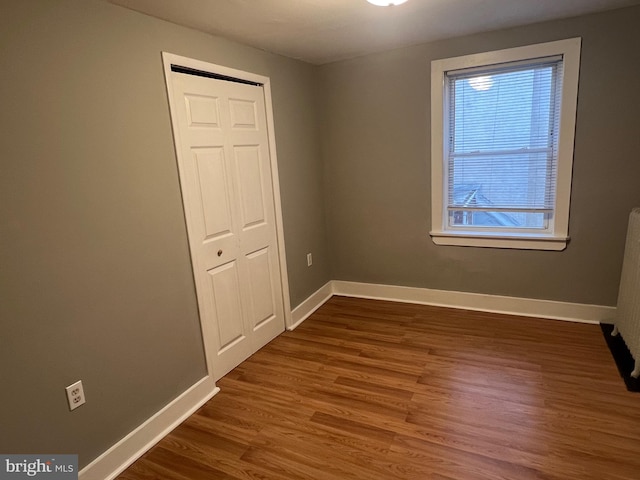 unfurnished bedroom featuring multiple windows, dark hardwood / wood-style floors, and a closet