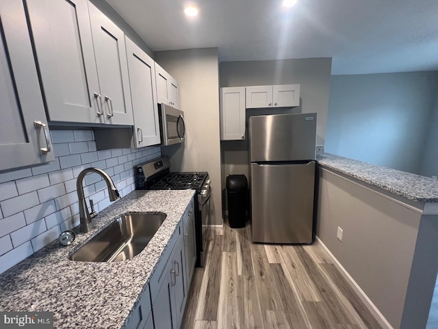 kitchen with sink, appliances with stainless steel finishes, tasteful backsplash, light stone countertops, and light hardwood / wood-style floors