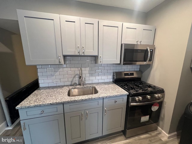 kitchen with tasteful backsplash, sink, light wood-type flooring, light stone countertops, and appliances with stainless steel finishes