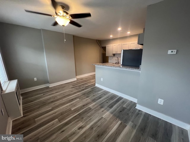 kitchen with tasteful backsplash, kitchen peninsula, sink, light stone countertops, and white cabinets