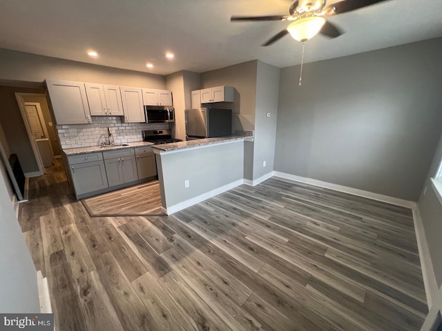 kitchen with kitchen peninsula, stainless steel appliances, dark hardwood / wood-style floors, tasteful backsplash, and sink