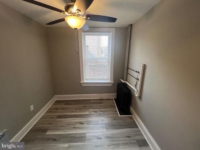 empty room with ceiling fan, dark wood-type flooring, and radiator heating unit