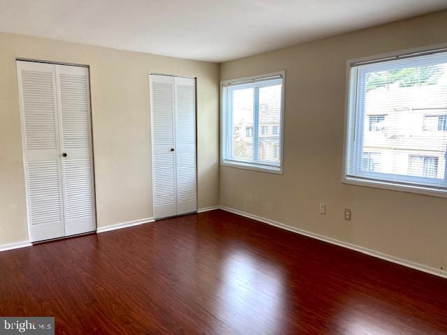 unfurnished bedroom with multiple closets and dark hardwood / wood-style floors