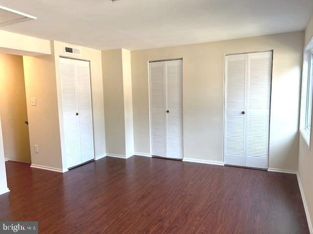 unfurnished bedroom with dark hardwood / wood-style flooring and two closets