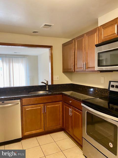 kitchen with stainless steel appliances, sink, light tile patterned floors, and dark stone counters