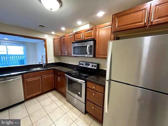 kitchen with dark stone countertops, stainless steel appliances, sink, and light tile patterned floors