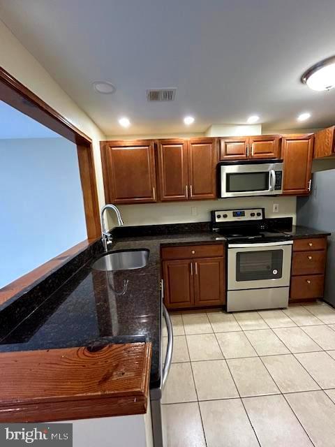 kitchen with stainless steel appliances, light tile patterned flooring, sink, and dark stone countertops