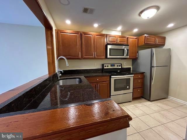 kitchen with sink, dark stone countertops, light tile patterned floors, kitchen peninsula, and stainless steel appliances