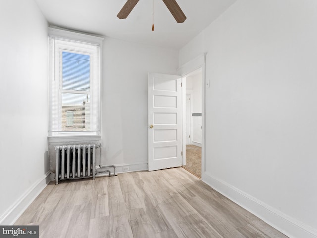 unfurnished room featuring ceiling fan, radiator, light wood-type flooring, and plenty of natural light