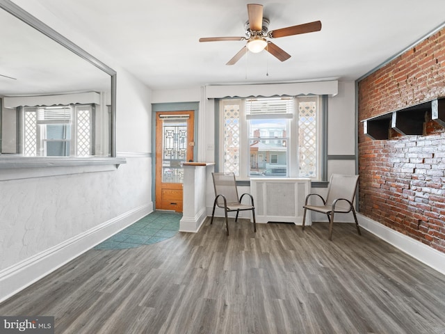 interior space with ceiling fan, dark wood-type flooring, and brick wall