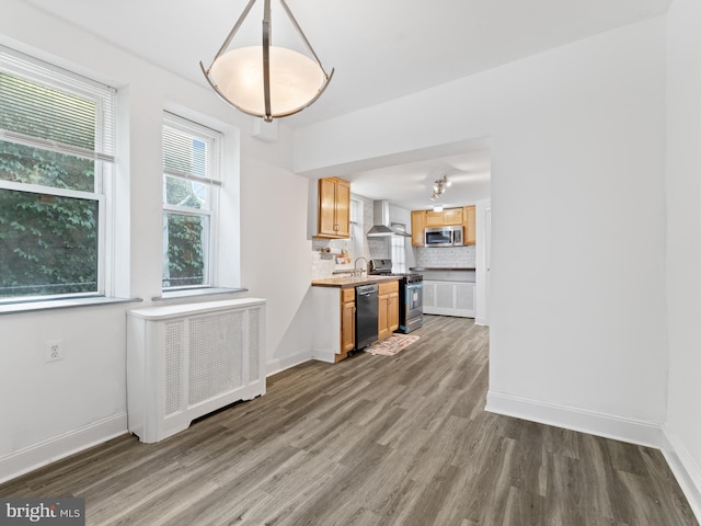 interior space with appliances with stainless steel finishes, tasteful backsplash, hanging light fixtures, wall chimney range hood, and radiator