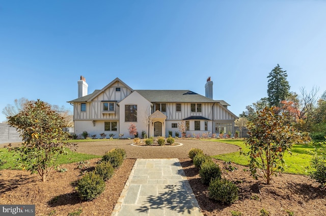 tudor house with a chimney, a front lawn, and board and batten siding