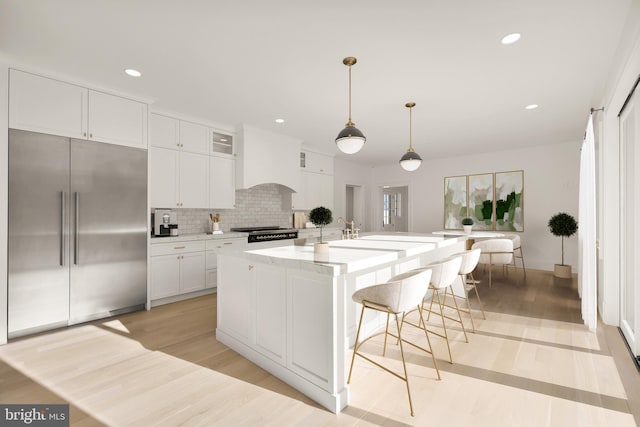 kitchen featuring a center island with sink, tasteful backsplash, built in fridge, hanging light fixtures, and white cabinets