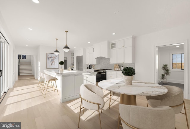 kitchen featuring premium range hood, white cabinetry, a center island with sink, range with two ovens, and hanging light fixtures