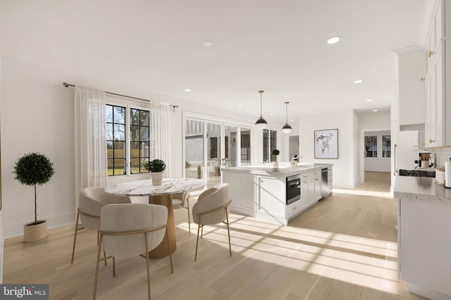 kitchen with light hardwood / wood-style flooring, an island with sink, white cabinetry, and pendant lighting