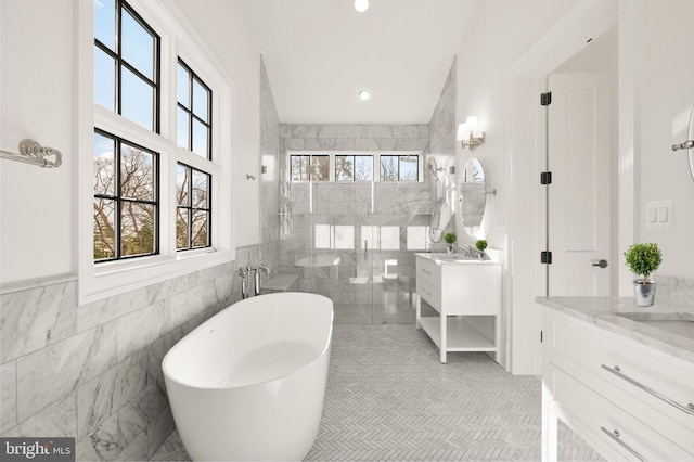 full bathroom with recessed lighting, two vanities, tile walls, a soaking tub, and a tile shower