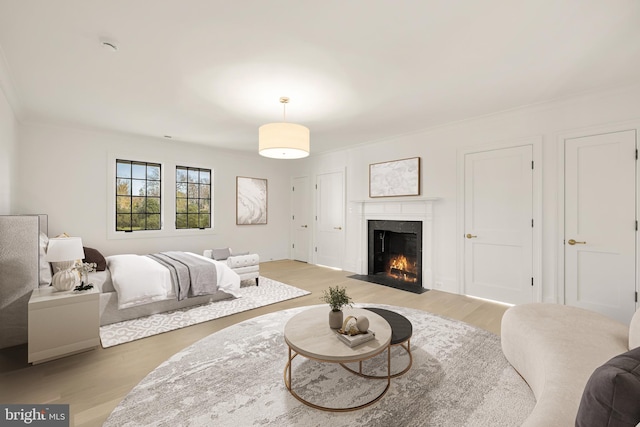 bedroom featuring a fireplace with flush hearth, crown molding, and light wood-style flooring