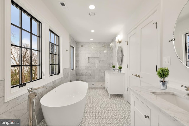 full bathroom with tile walls, two vanities, a sink, a freestanding tub, and tiled shower