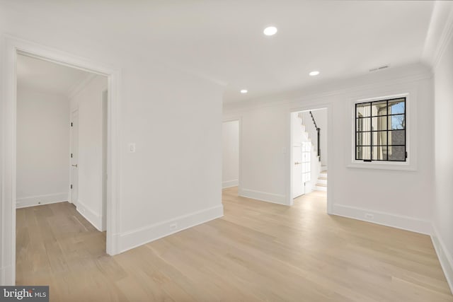 empty room with light wood-style flooring, visible vents, baseboards, stairway, and crown molding