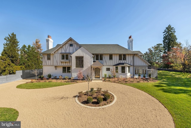 tudor house with curved driveway, a chimney, board and batten siding, a front yard, and fence