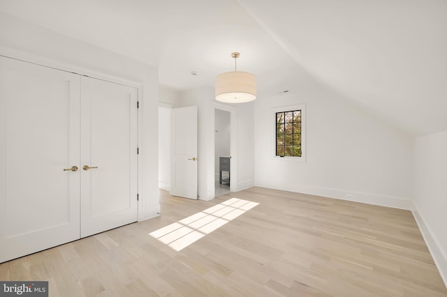 unfurnished bedroom featuring lofted ceiling, a closet, and light hardwood / wood-style floors