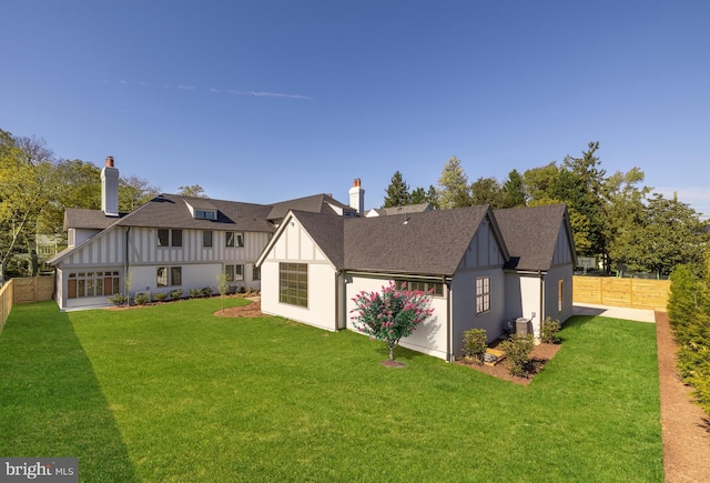 rear view of house with roof with shingles, a lawn, and fence