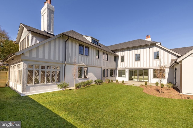 rear view of property featuring a yard, a chimney, a shingled roof, board and batten siding, and a sunroom