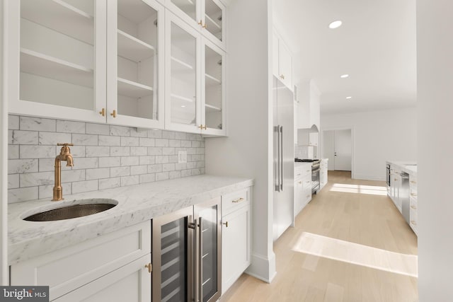 kitchen with glass insert cabinets, white cabinetry, a sink, light stone countertops, and beverage cooler