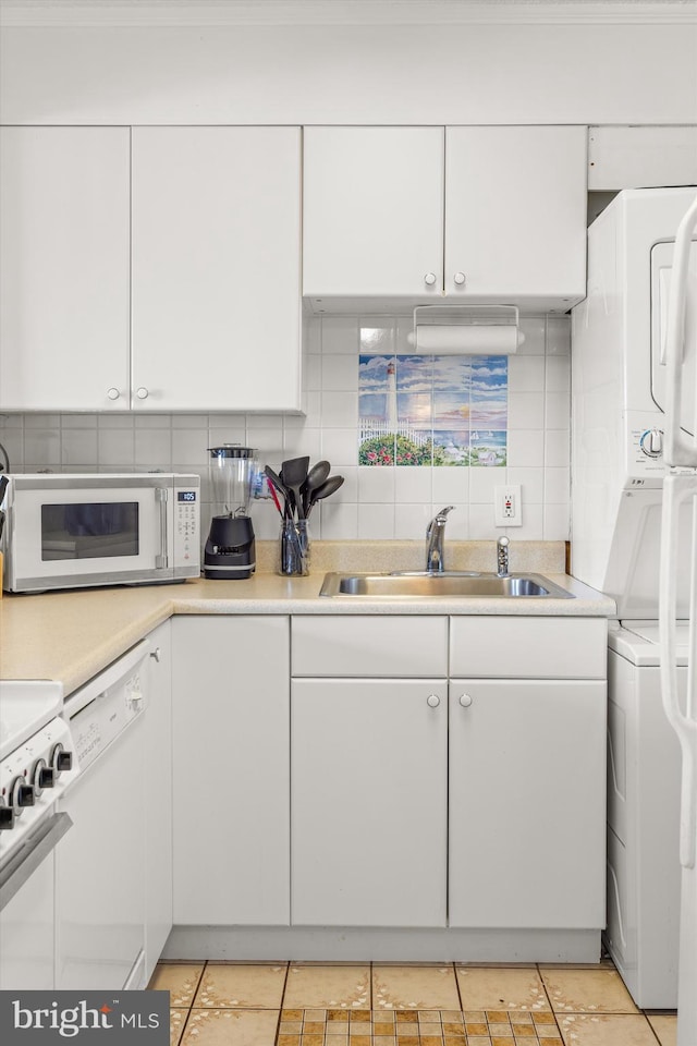 kitchen featuring stacked washer and dryer, white appliances, sink, white cabinetry, and backsplash