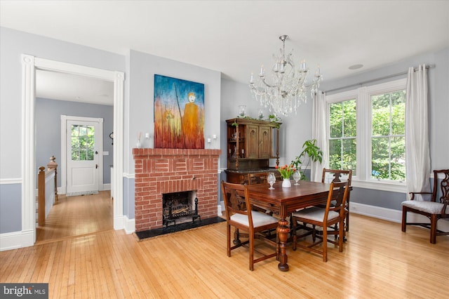 dining room featuring a healthy amount of sunlight, light hardwood / wood-style floors, a brick fireplace, and a chandelier