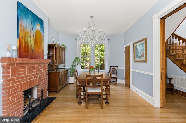 dining area featuring light hardwood / wood-style flooring, a brick fireplace, and a chandelier