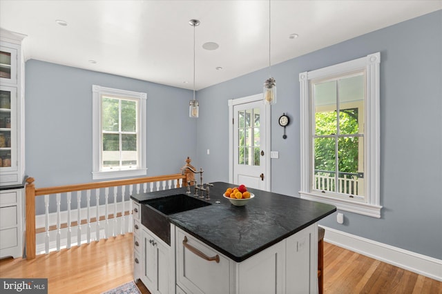 kitchen with light hardwood / wood-style flooring, white cabinets, an island with sink, hanging light fixtures, and sink