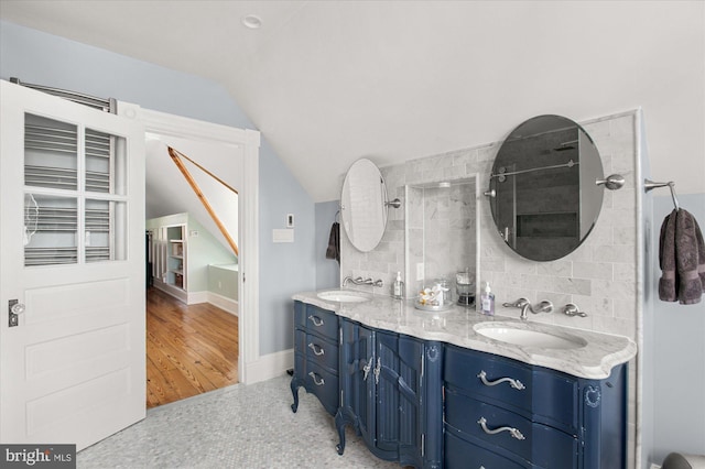 bathroom with decorative backsplash, hardwood / wood-style flooring, dual vanity, and vaulted ceiling