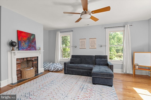 living room with a healthy amount of sunlight, light hardwood / wood-style floors, a brick fireplace, and ceiling fan