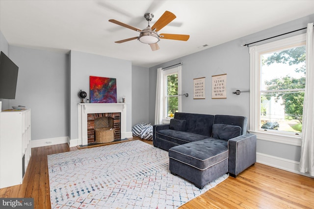 living room with ceiling fan, light hardwood / wood-style flooring, and a brick fireplace