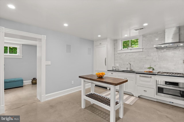 kitchen with wall chimney range hood, stainless steel appliances, a healthy amount of sunlight, and white cabinets