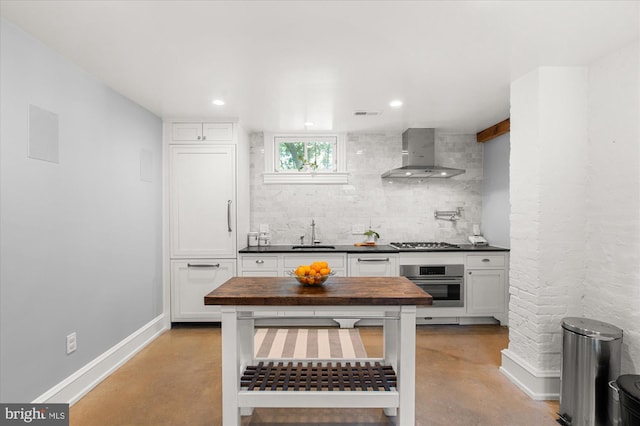 kitchen featuring white cabinets, stainless steel appliances, sink, butcher block counters, and wall chimney exhaust hood