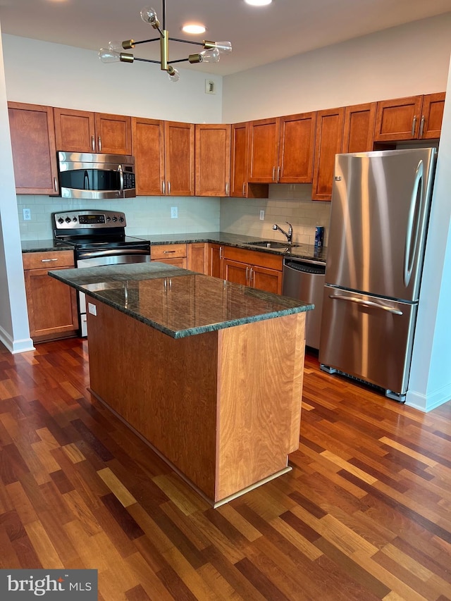 kitchen featuring appliances with stainless steel finishes, a kitchen island, dark hardwood / wood-style flooring, dark stone countertops, and sink