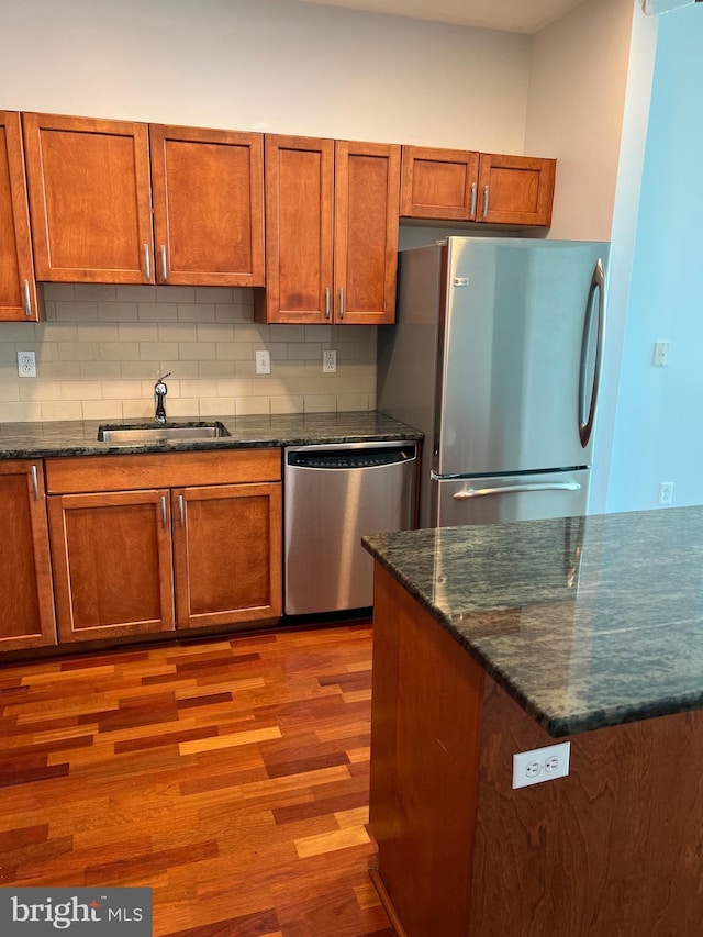 kitchen with tasteful backsplash, sink, light hardwood / wood-style flooring, appliances with stainless steel finishes, and dark stone counters