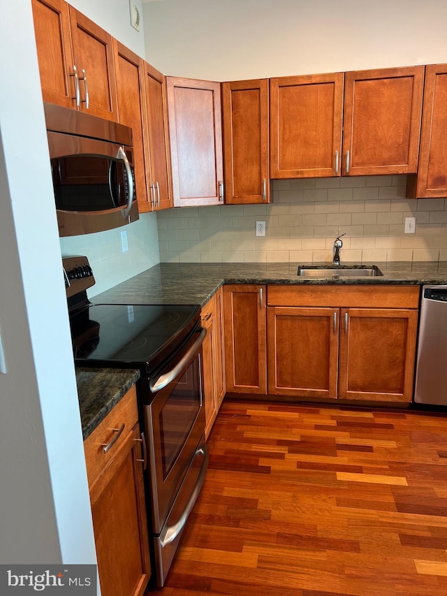 kitchen featuring appliances with stainless steel finishes, dark wood-type flooring, dark stone countertops, sink, and backsplash