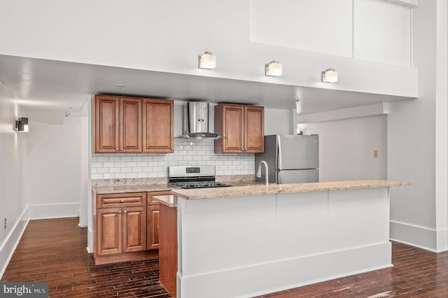 kitchen featuring an island with sink, appliances with stainless steel finishes, tasteful backsplash, dark hardwood / wood-style flooring, and wall chimney range hood