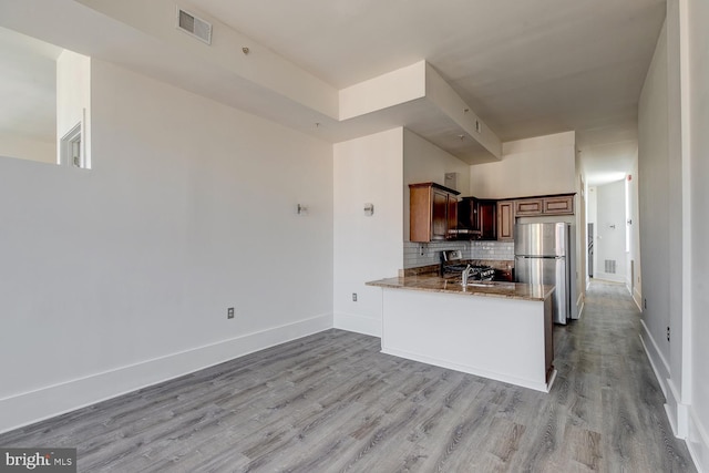 kitchen featuring backsplash, kitchen peninsula, light hardwood / wood-style flooring, stainless steel fridge, and stone countertops