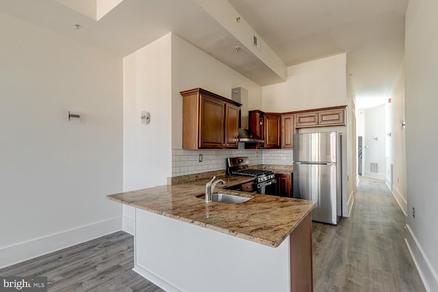 kitchen featuring kitchen peninsula, decorative backsplash, sink, light stone countertops, and appliances with stainless steel finishes